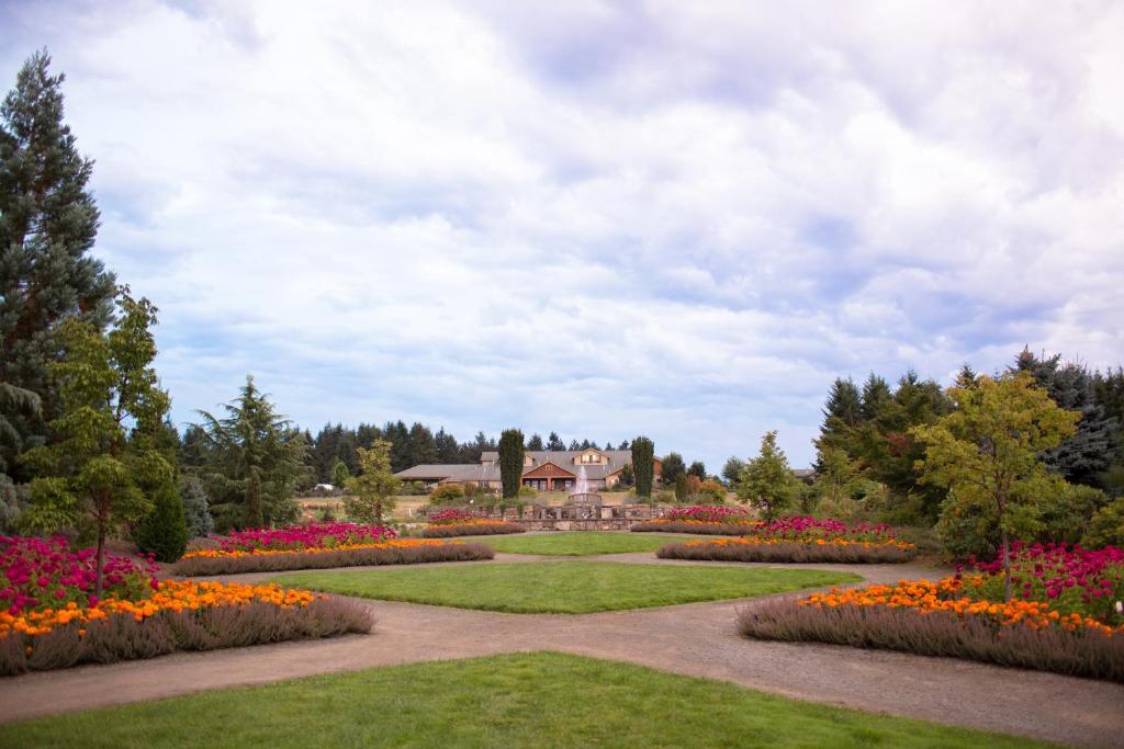 Oregon Garden Resort في سيلفيرتون: حديقة بها زهور ومنزل في الخلفية