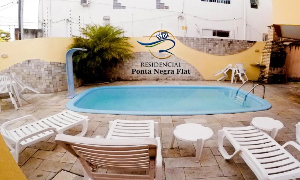 a swimming pool with chairs and a table and a sign at Residencial Ponta Negra Flat in Natal