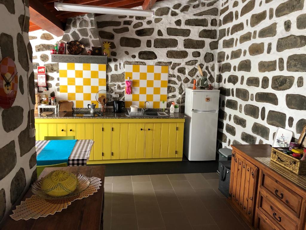 a kitchen with yellow cabinets and a stone wall at Casa Auri in Faial da Terra