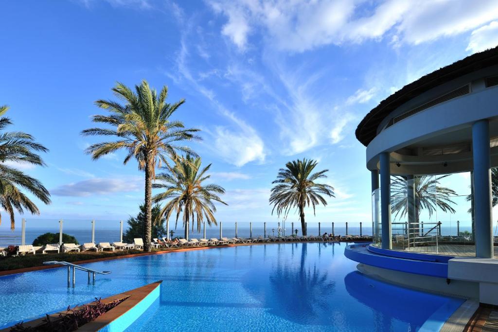 uma piscina com palmeiras e um edifício em Pestana Grand Ocean Resort Hotel em Funchal