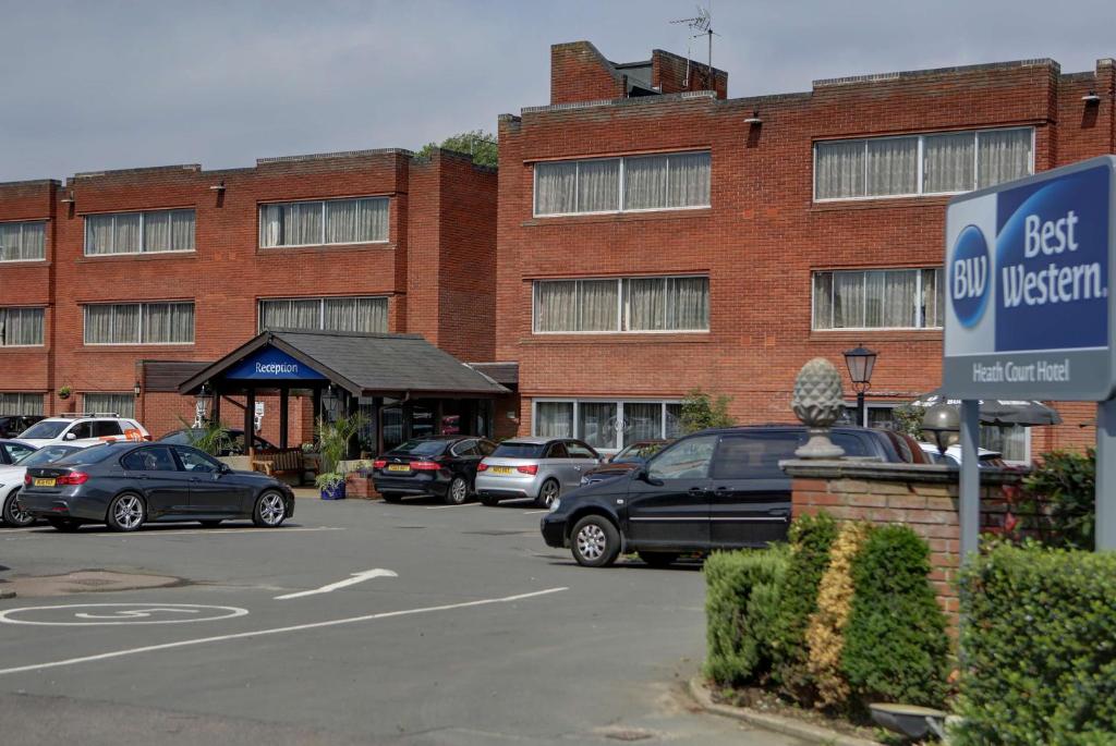 un estacionamiento con autos estacionados frente a un edificio en Best Western Heath Court Hotel, en Newmarket