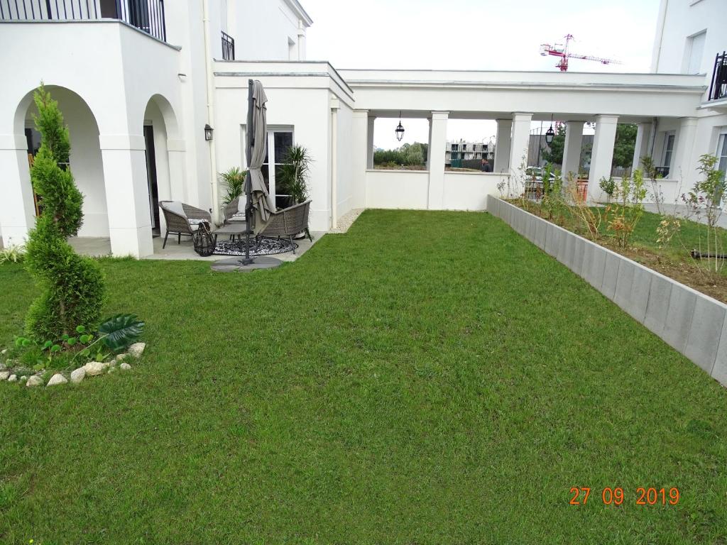 une cour avec de l'herbe verte devant une maison blanche dans l'établissement Victoria Family House Disneyland Paris, à Serris