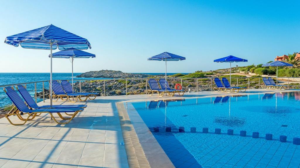 Una piscina con sillas y sombrillas junto al mar. en Vlamis Villas, en Stavros