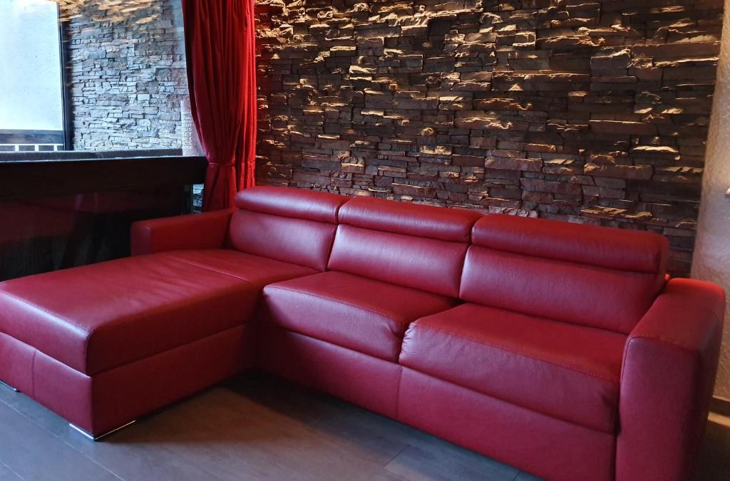 czerwona skórzana kanapa w pokoju z ceglaną ścianą w obiekcie Le Serac W6 appartement avec véranda en angle vue panoramique gérer par particulier sur place w Val Thorens