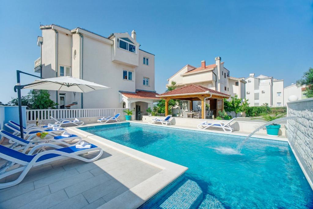 a swimming pool with chairs and an umbrella and some buildings at Apartments Plavi Biser in Šibenik