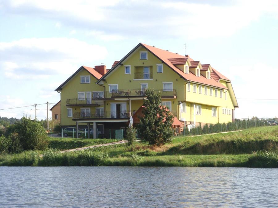 a large yellow house on a hill next to a body of water at Hotel Pod Jaskółką in Kołomań