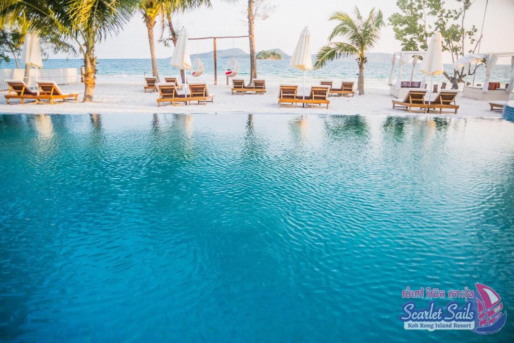 a swimming pool with chairs and the ocean in the background at Scarlet Sails Resort in Koh Rong Island