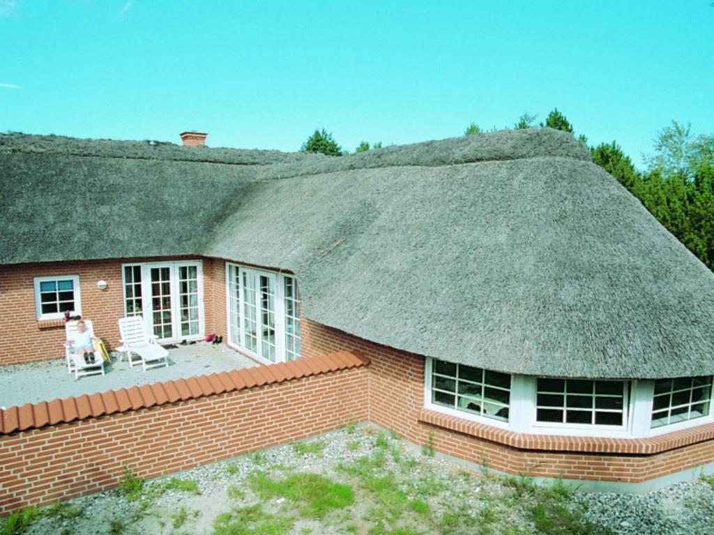 a thatch roofed house with a dog sitting on a patio at Six-Bedroom Holiday home in Væggerløse 3 in Marielyst