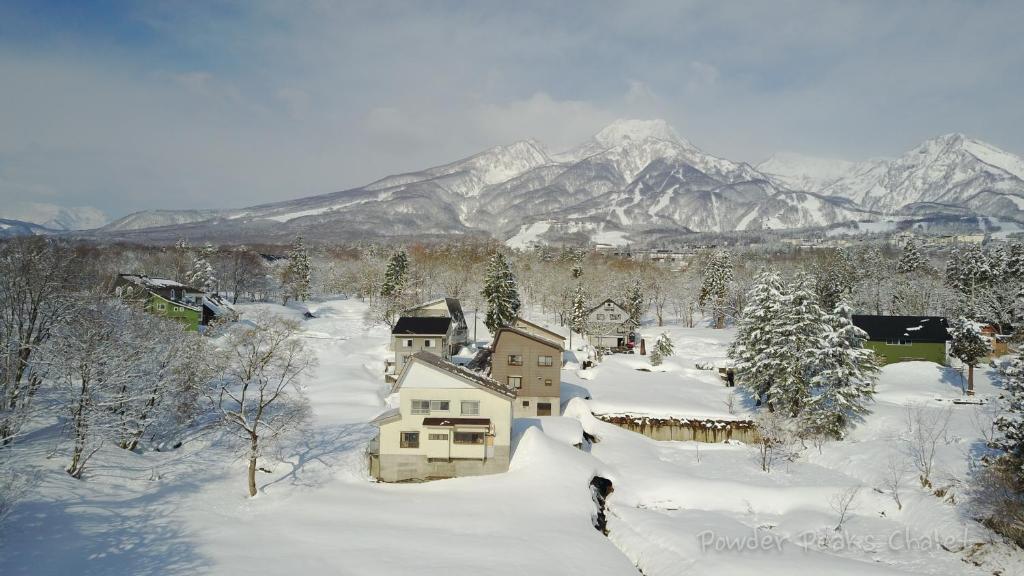 a house covered in snow with mountains in the background at Powder Peaks Chalet in Akakura