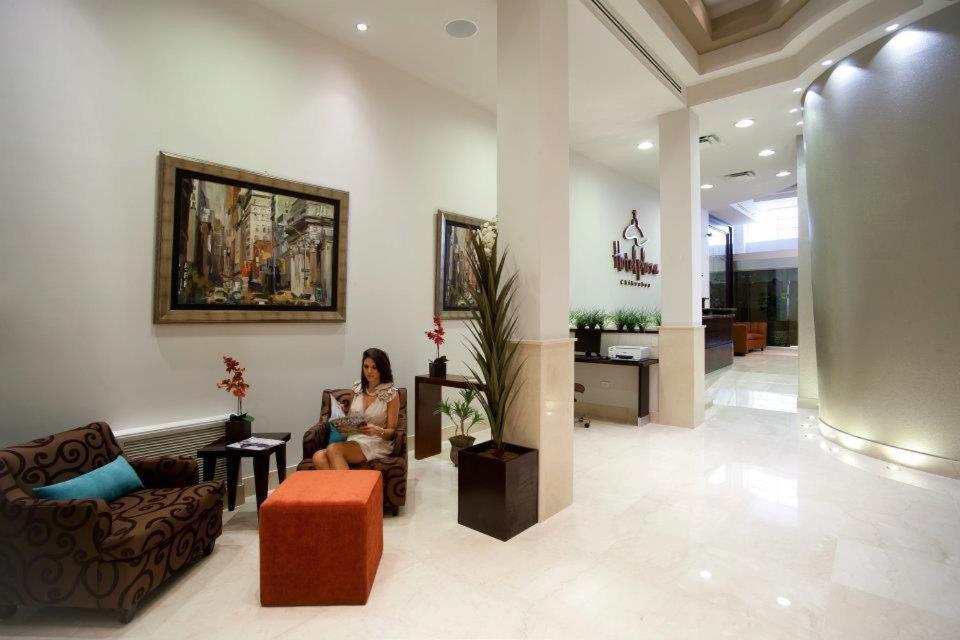 une femme assise sur une chaise dans un hall dans l'établissement Hotel Plaza Chihuahua, à Chihuahua