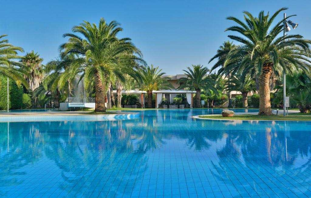 a swimming pool with palm trees and a building at Minerva Resort Hotel in Paestum