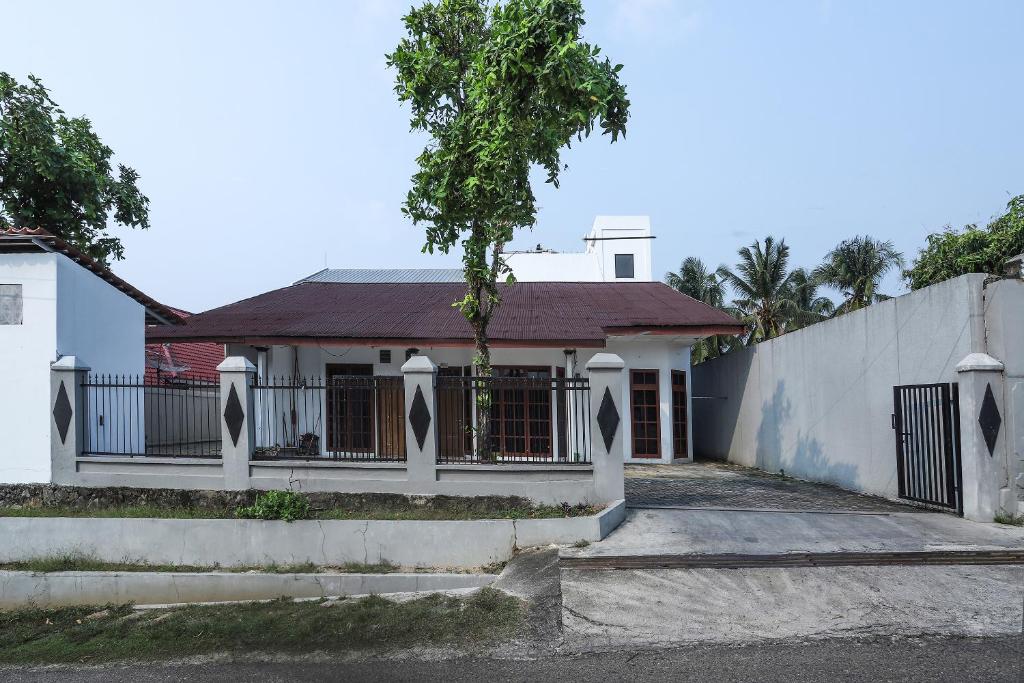 una casa blanca con una valla y un árbol en Super OYO 1582 Bungo Guest House, en Muarabungo