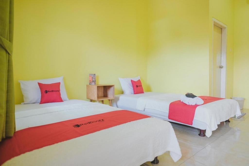 Cette chambre comprend 2 lits avec des draps rouges et blancs. dans l'établissement RedDoorz Syariah near Kantor Walikota Jambi, à Jambi