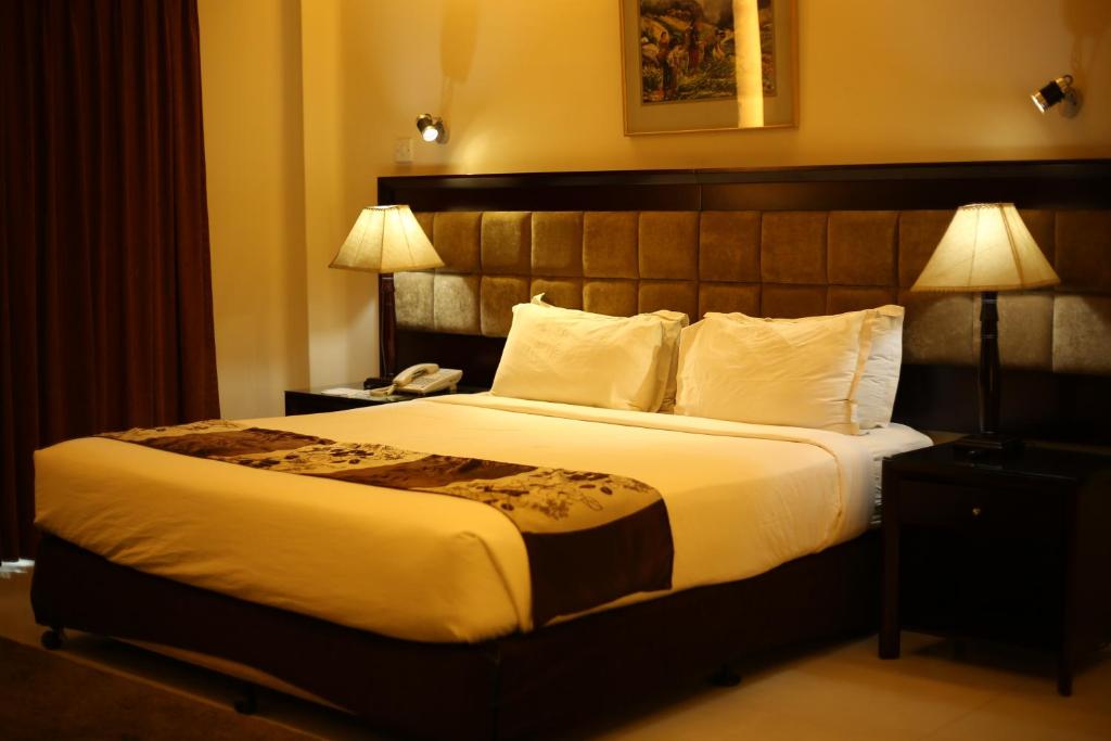 THE AVENUE HOTEL & SUITES في شيتاغونغ: غرفة فندقية بسرير كبير ومصباحين