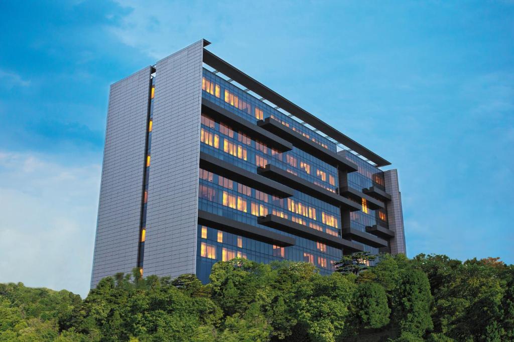 Un edificio alto con árboles delante. en Trident Hyderabad, en Hyderabad