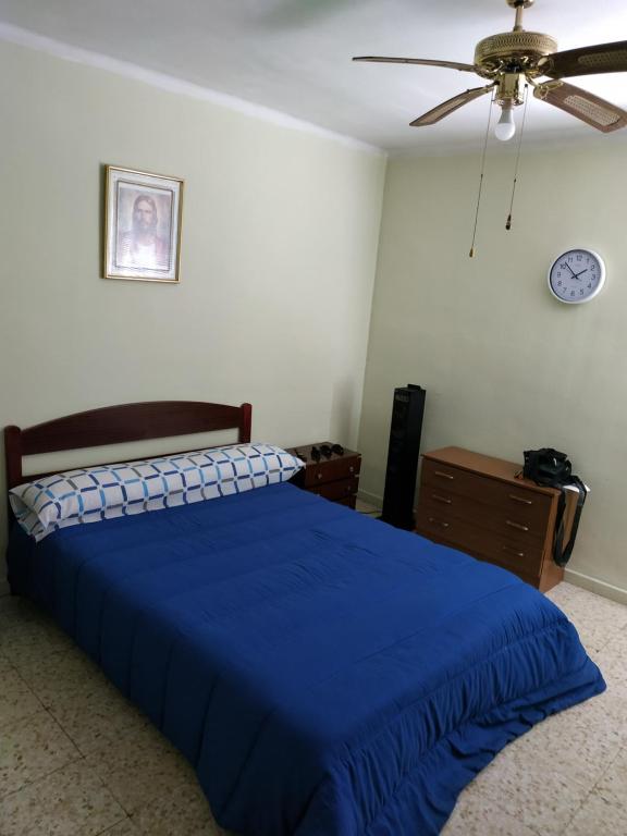 1 dormitorio con 1 cama azul y ventilador de techo en Habitación en piso particular 4 min.aeropuerto en Sevilla