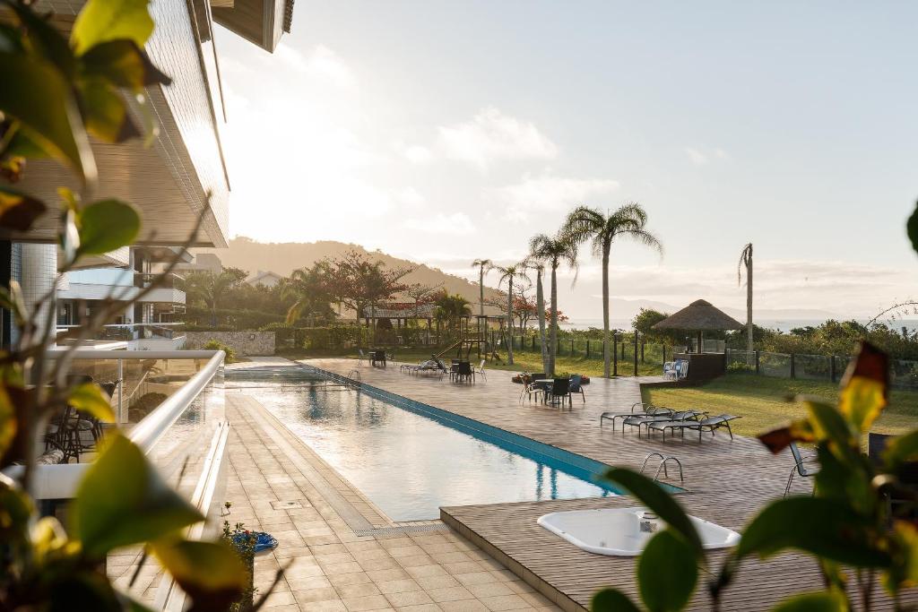 uma piscina com mesas e cadeiras e palmeiras em Apartamento com 4 suítes pé na areia em Florianópolis