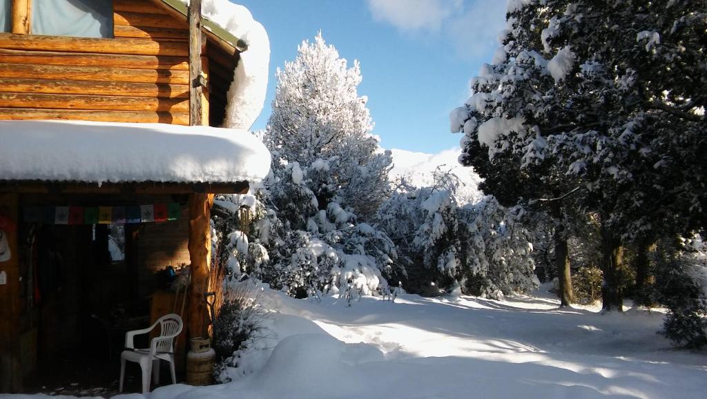 a log cabin in the snow with trees in the background at EL Arka in San Carlos de Bariloche