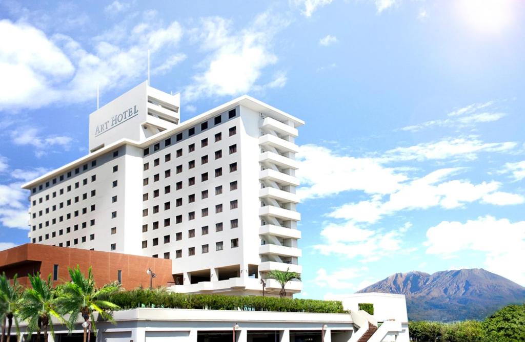 a large white building with a mountain in the background at Art Hotel Kagoshima in Kagoshima