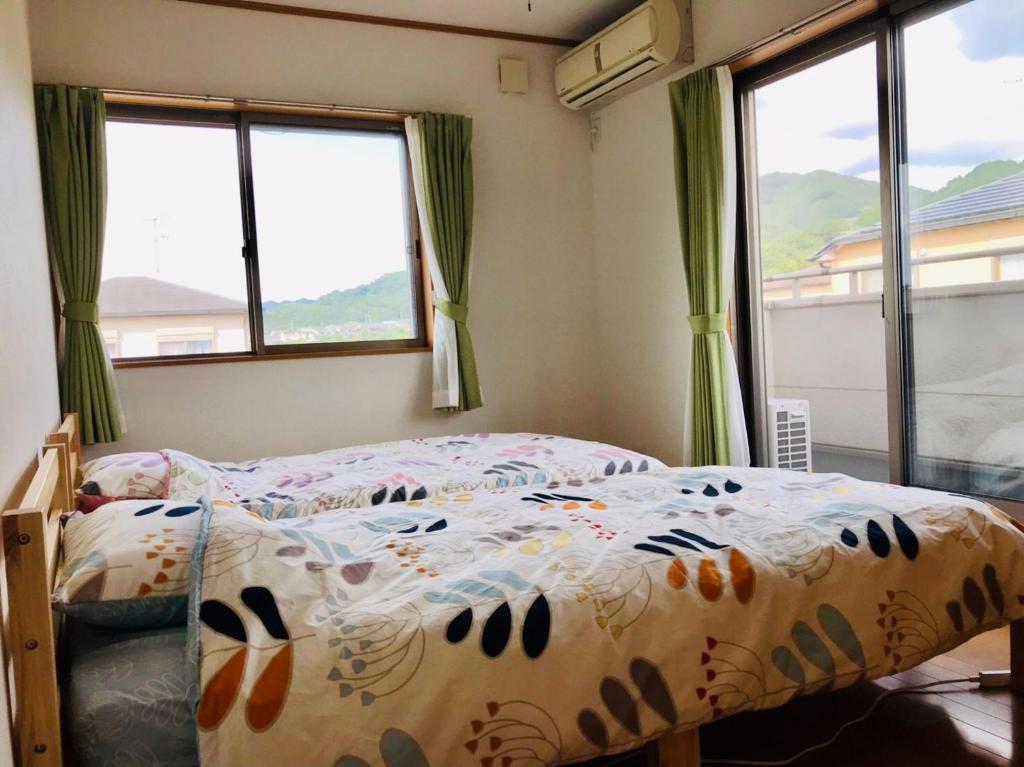 a bedroom with a bed with a comforter and windows at Yamanobenomichi teku teku in Tenri