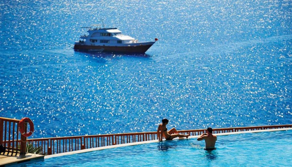 two people in a swimming pool with a boat in the water at Reef Oasis Blue Bay Resort & Spa in Sharm El Sheikh