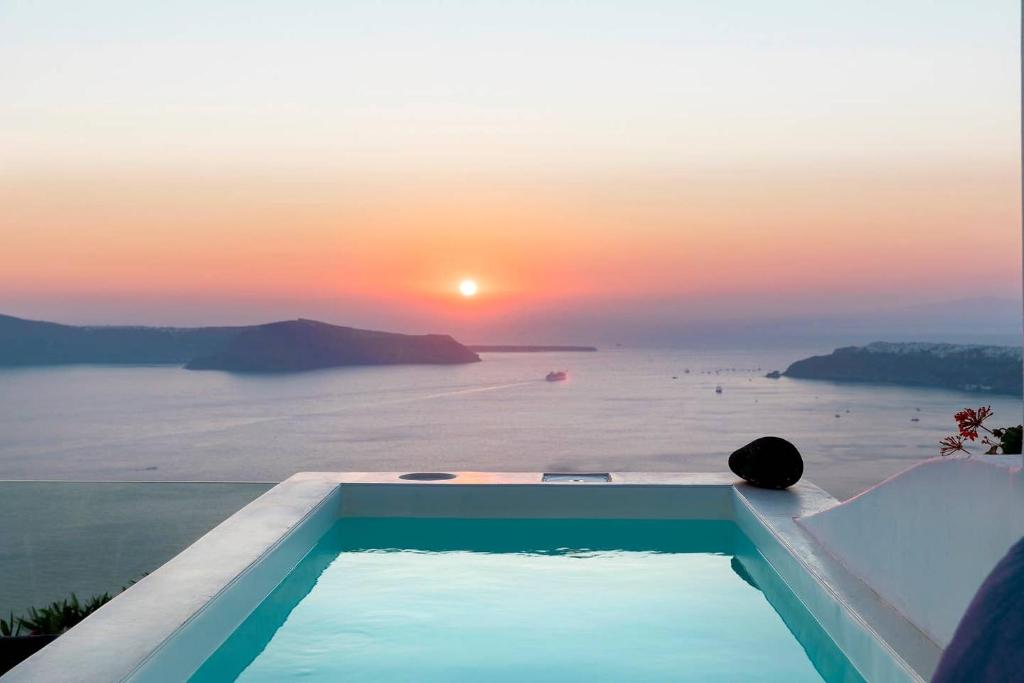 a pool with a view of the ocean at sunset at Aether Suite by Caldera Houses in Imerovigli