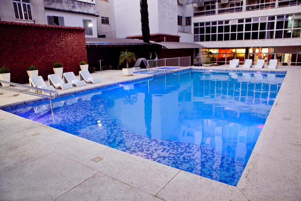 a large swimming pool with white chairs and a building at Ritz Plaza Hotel in Juiz de Fora