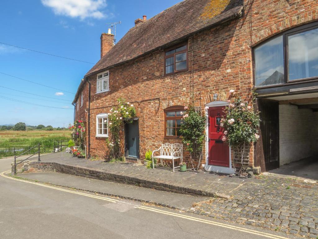 a brick house with a red door and flowers at River Cottage in Tewkesbury