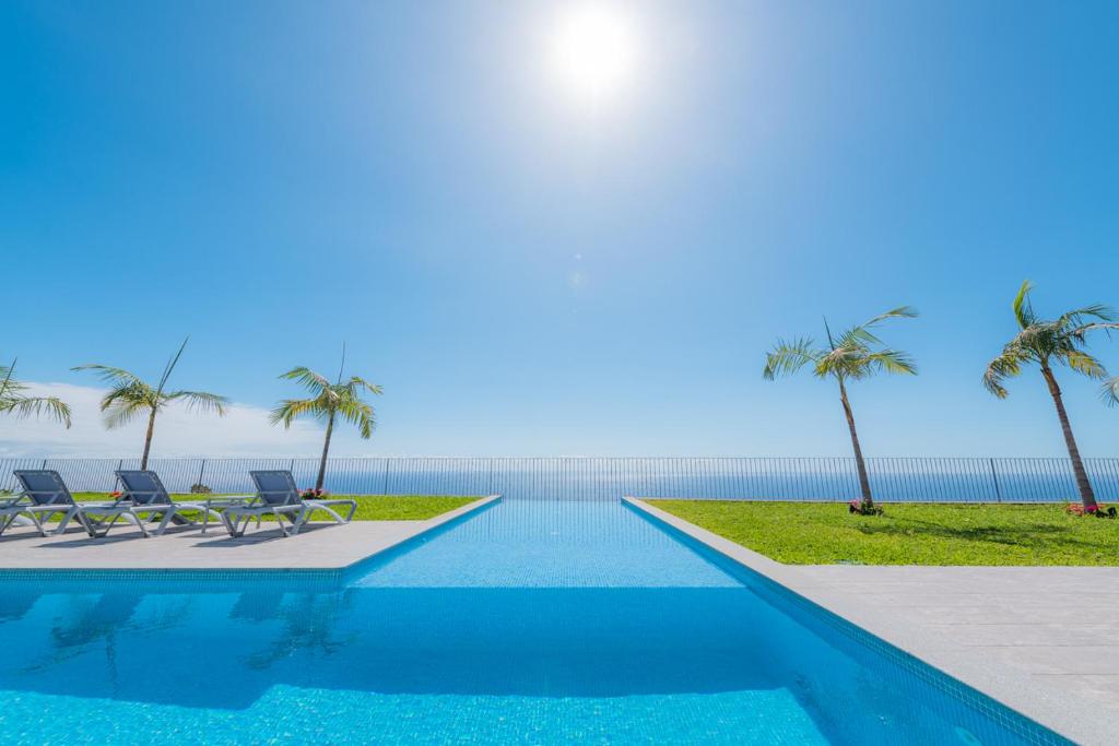 a swimming pool with two chairs and palm trees at Engenho Velho Hotel. Restaurante in Arco da Calheta