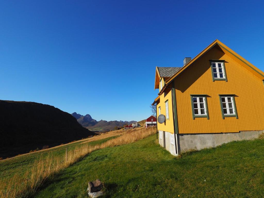 une maison jaune sur une colline avec un champ vert dans l'établissement Lofoten Hiking Lodge, à Bøstad