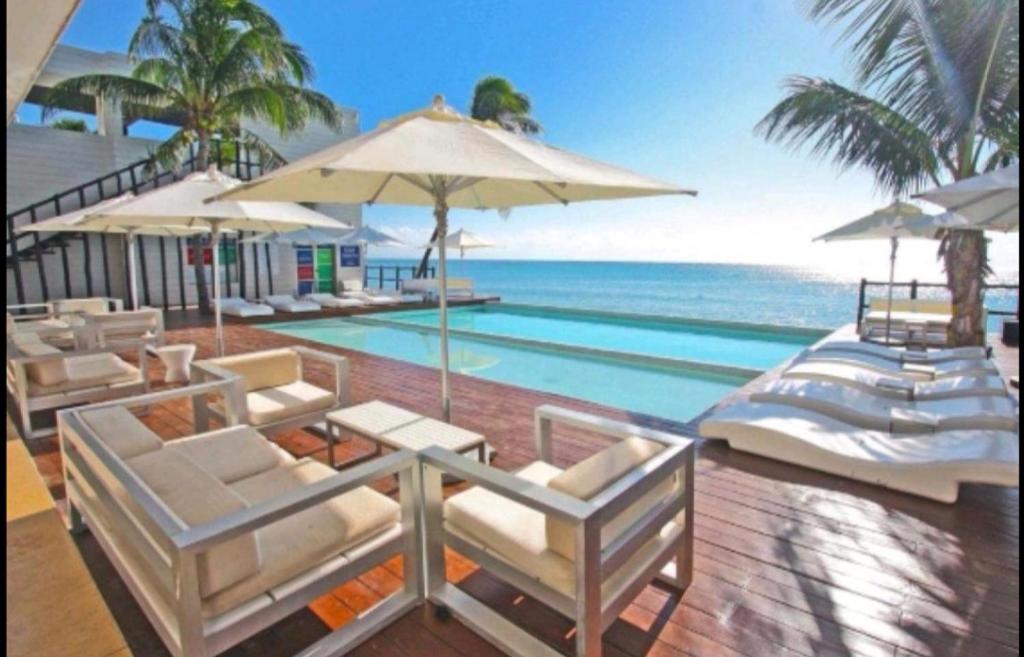una piscina con sillas y una sombrilla y el océano en Beachside Resplandor Maya Corasol with balcony for 4 people, en Playa del Carmen