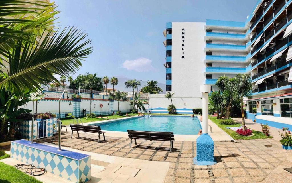 een zwembad met twee banken en een gebouw bij Cómodo estudio Playa Jardin in Puerto de la Cruz