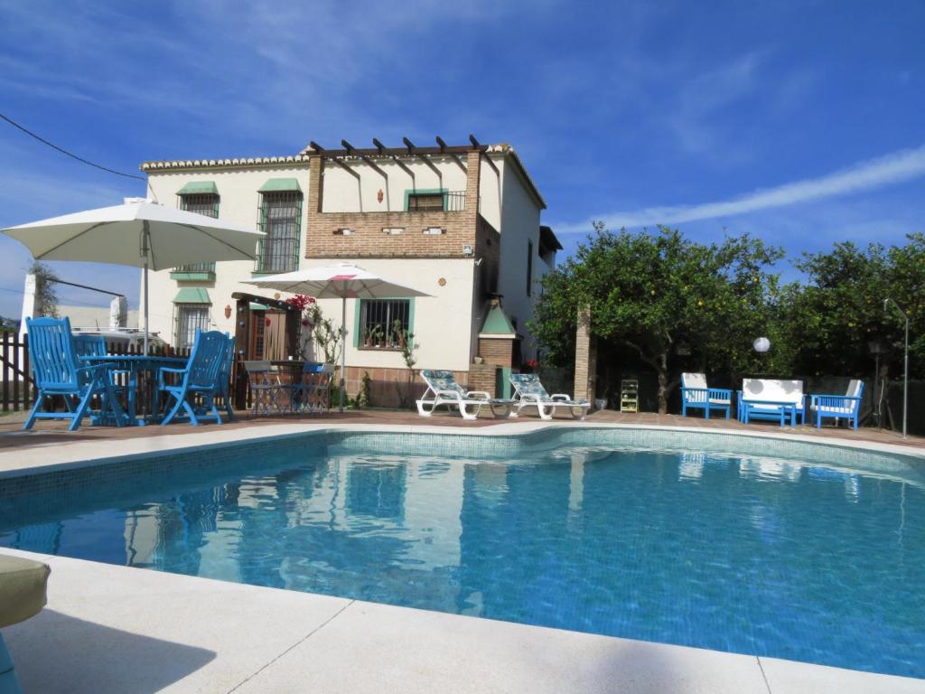 a swimming pool with blue chairs and a house at Casa rural la Estrella in Pizarra