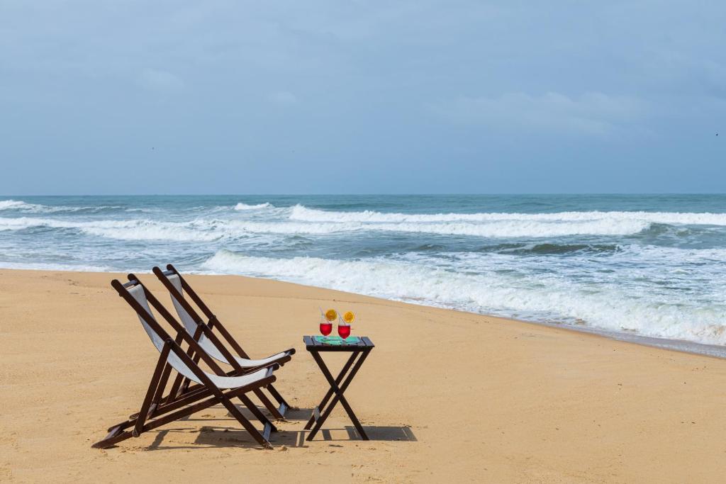 2 sillas y una mesa en la playa en SaffronStays Blue Flag House, a 3-BDR beachfront villa in Hejamady, en Mangalore