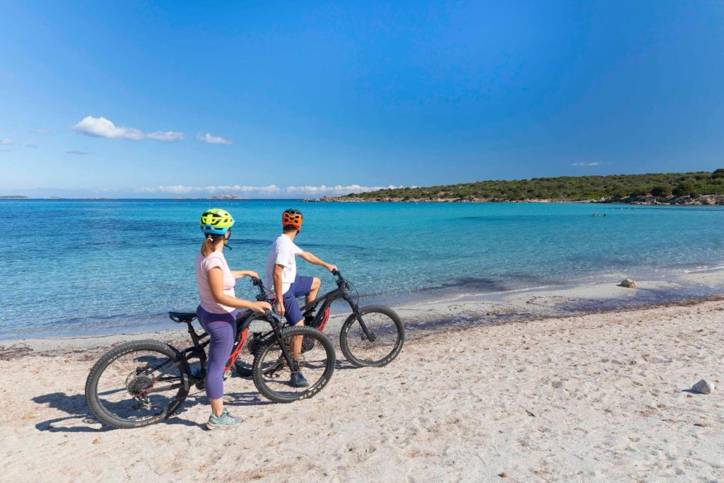 two people riding bikes on the beach at Hotel Abi d'Oru in Porto Rotondo