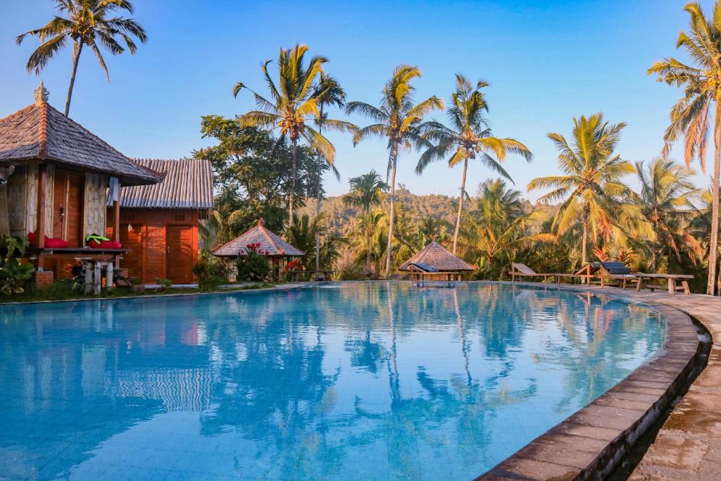 a swimming pool at a resort with palm trees in the background at Puri Sunny Camp in Munduk