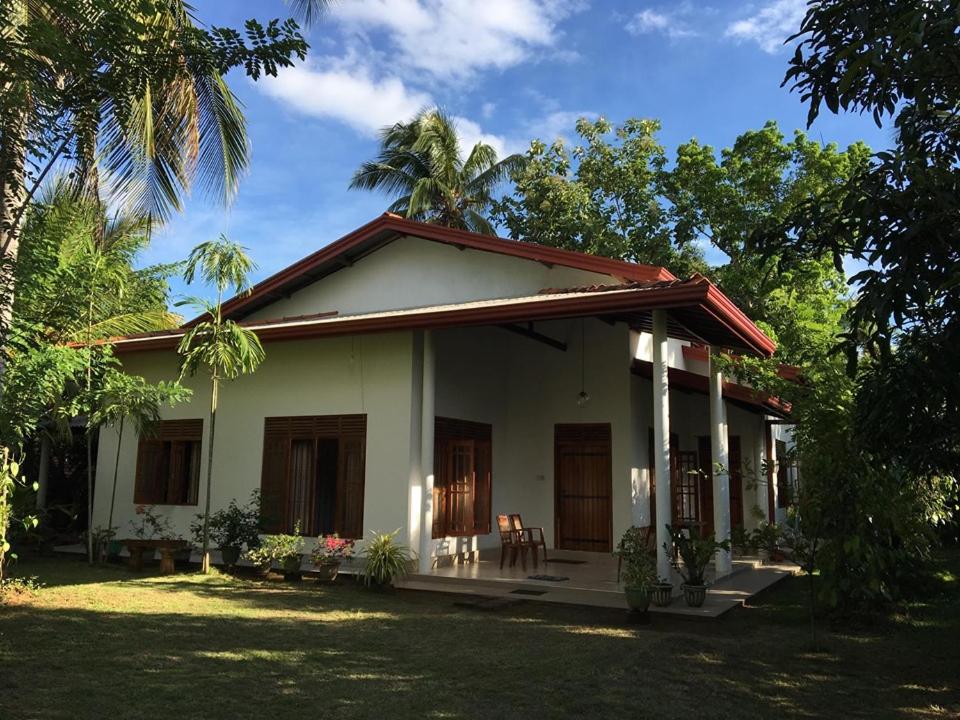 a small white house with a porch and trees at Serene Home Stay in Udawalawe