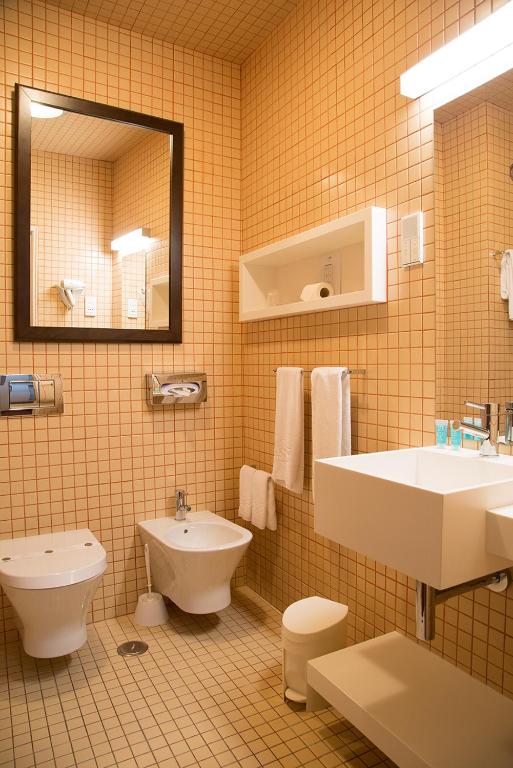 A fully tiled bathroom with a wall-mounted sink, bidet, toilet and open recessed shelving.