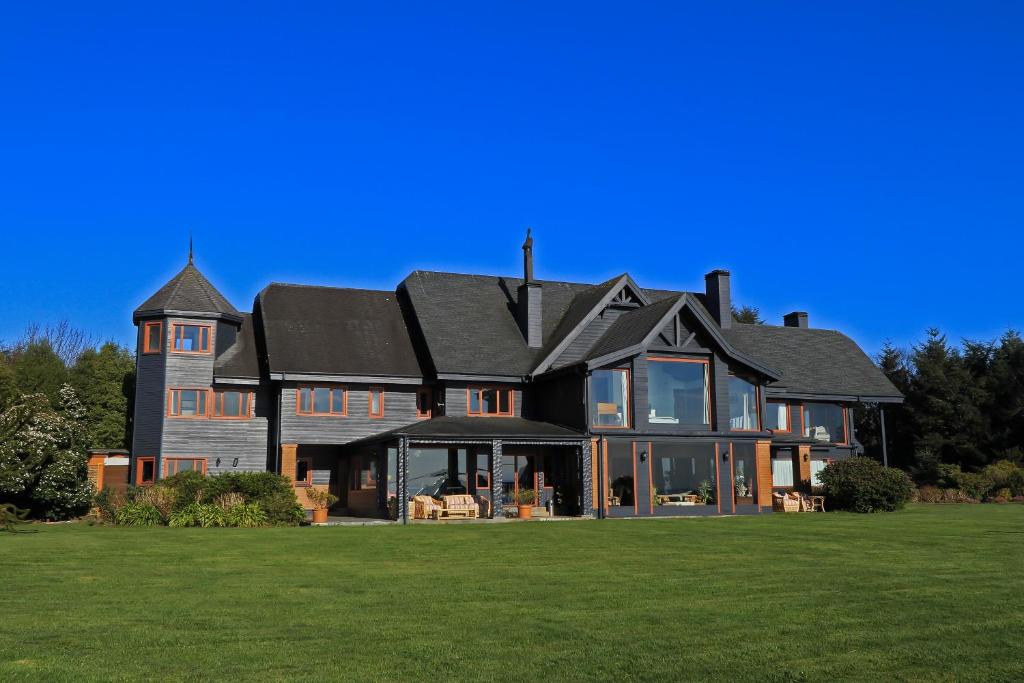 a large house with a black roof on a green field at Casa Molino Hotel Boutique & Restaurant Puerto Varas in Puerto Varas