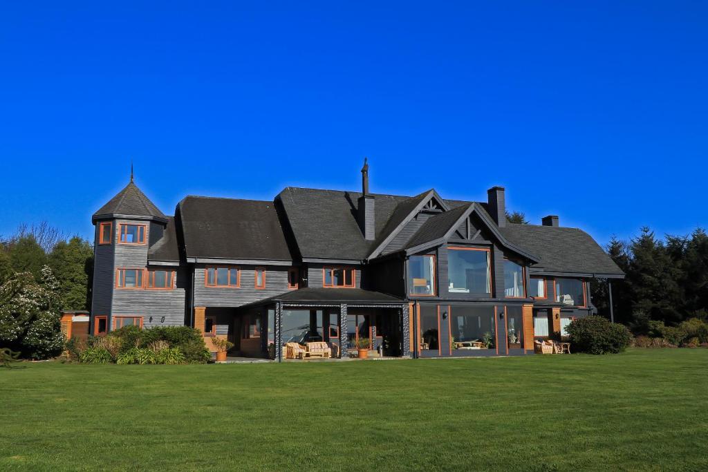 a large house with a black roof on a green field at Casa Molino Hotel Boutique & Restaurant in Puerto Varas
