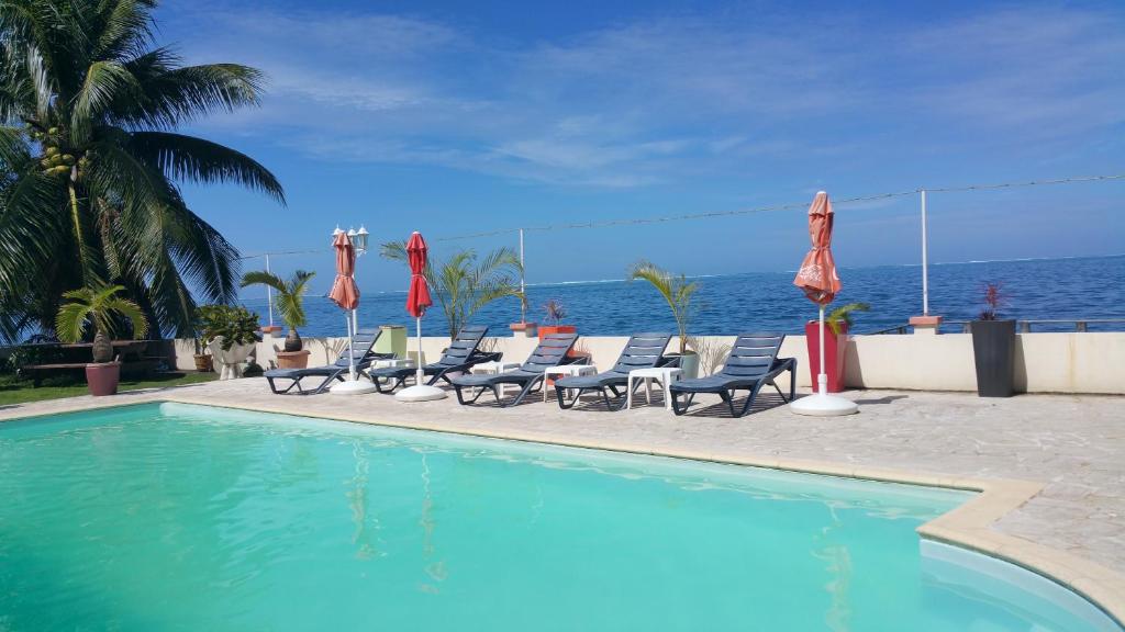 a swimming pool with chairs and umbrellas and the ocean at Pension de famille HITI MOANA VILLA in Papara