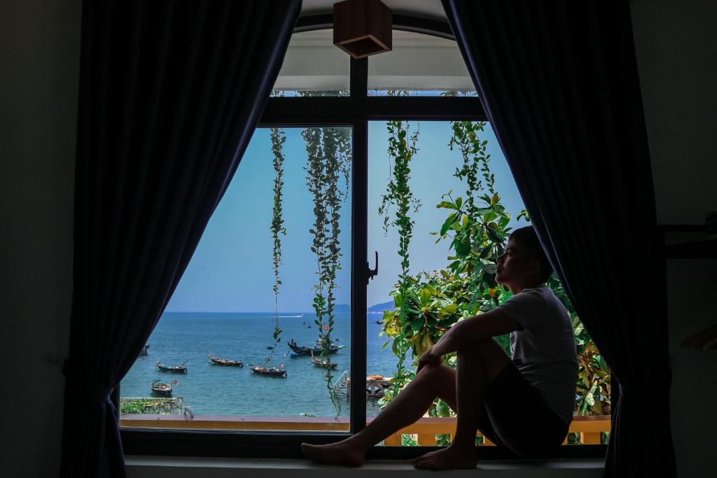 a woman sitting in a window looking out at the ocean at Sunbay Homestay Cu Lao Cham in Tân Hiệp