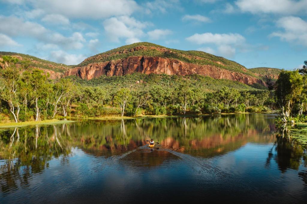 a person in a boat on a lake with a mountain at Mt Mulligan Lodge in Mount Mulligan