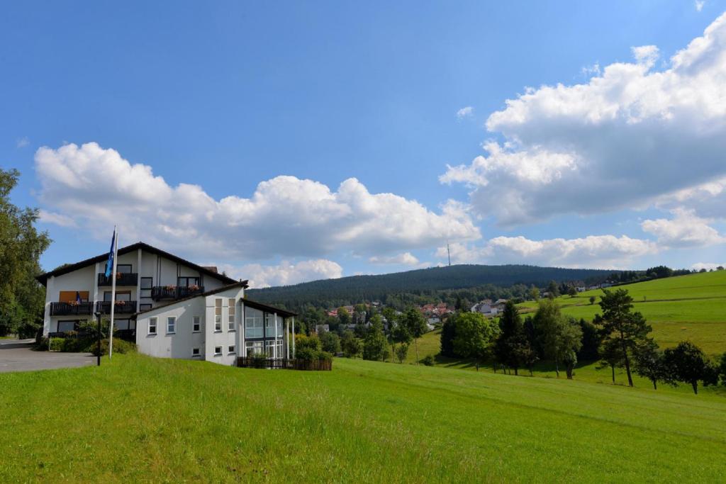 una casa en una colina con un campo verde en Hotel garni Siebenstern en Bischofsgrün