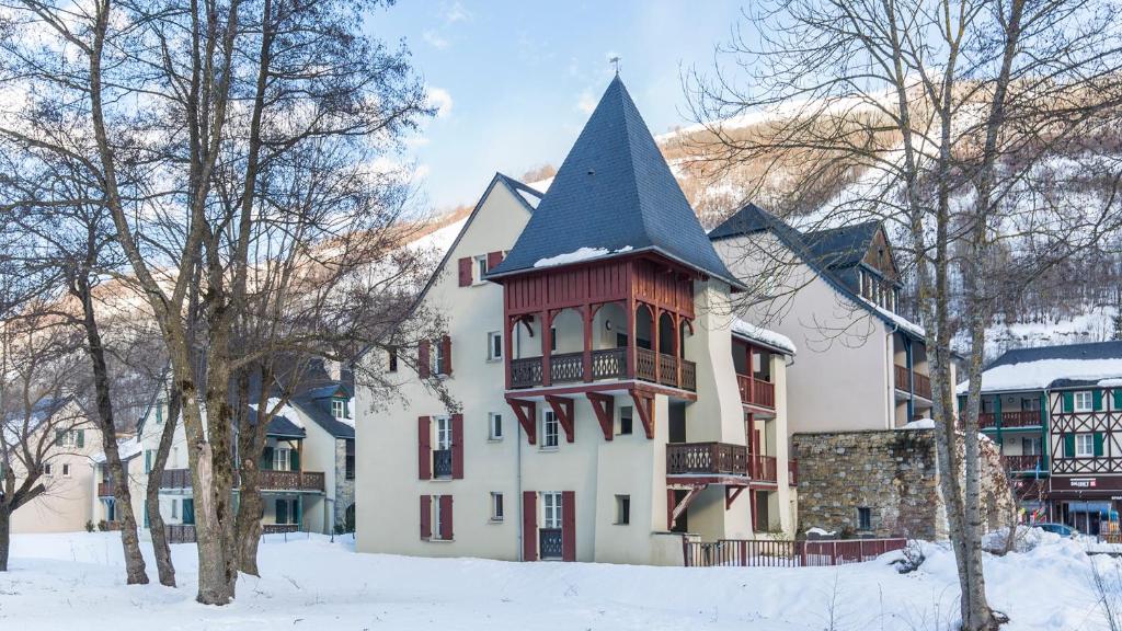 un grand bâtiment blanc avec une tourelle dans la neige dans l'établissement Vacancéole - Les Jardins de Balnéa, à Loudenvielle