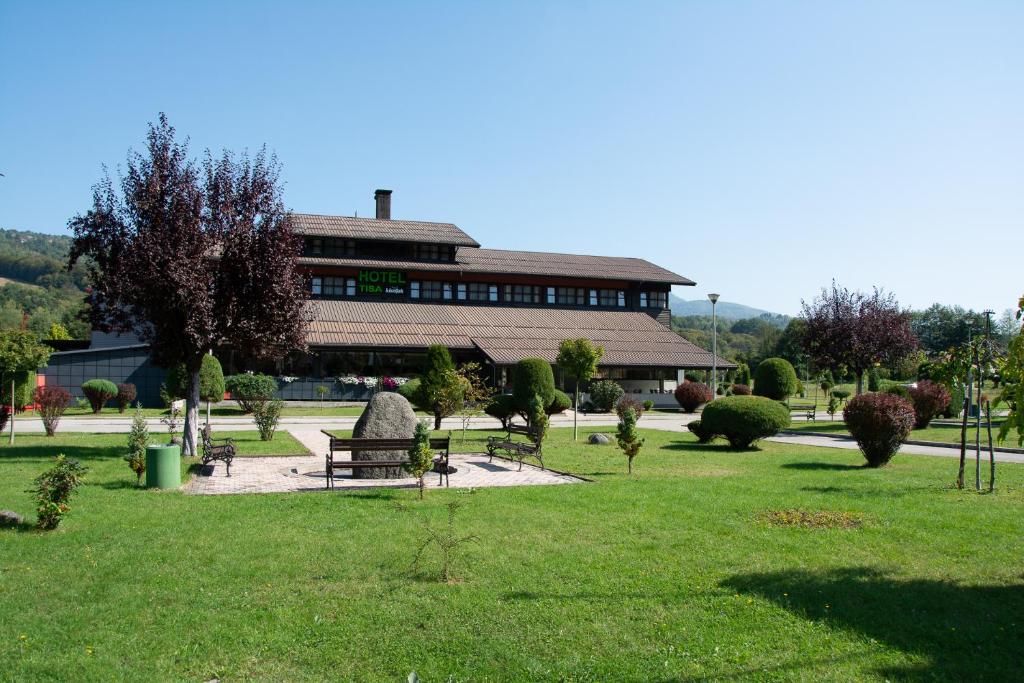 a building with a park with a bench in the grass at Hotel TISA in Busovača