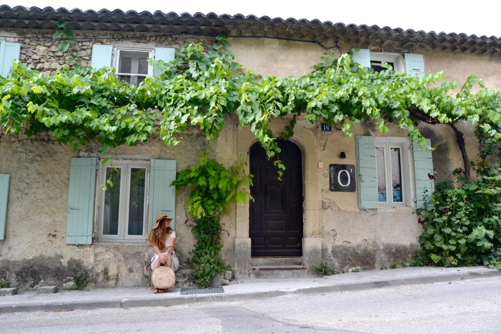 una mujer sentada frente a una casa con una puerta en Les Maisons du O, en Vaison-la-Romaine