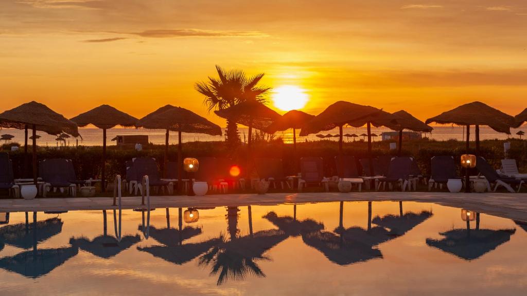 a pool with the sun setting in the background at Hotel Nour Congress & Resort in Bizerte