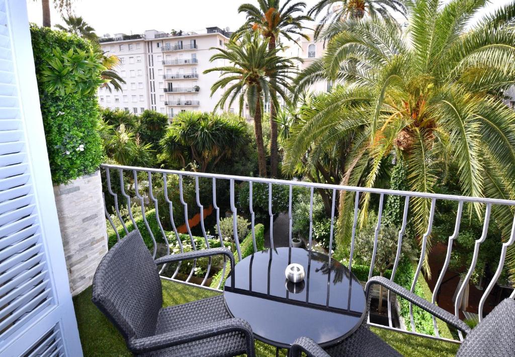a balcony with chairs and a table and palm trees at Hôtel de Provence in Cannes