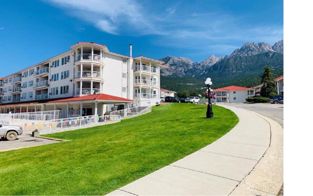 a building on a green lawn with mountains in the background at Mountain View Resort and Suites at Fairmont Hot Springs in Fairmont Hot Springs